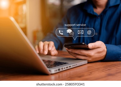 Customer support concept. Man using smartphone and laptop with virtual chat icons for email, phone, and AI chatbot assistance in business communication.