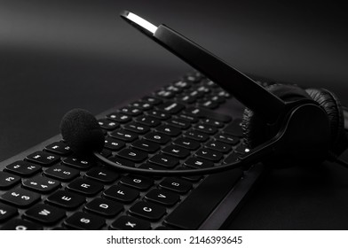 Customer Support Operator, Remote Call Center And Telephone Scam Concept With Headset With Microphone On Black Keyboard In A Ominous Dark Office With No People
