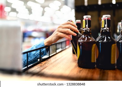 Customer Taking Bottle Of Beer From Shelf In Liquor Store. Woman Shopping Alcohol Or Supermarket Staff Filling And Stocking Shelves In Drink Aisle. Cider, Lager Or Dark. Retail Worker Doing Inventory.