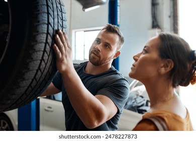 Customer, tire and mechanic in garage for maintenance, inspection and car service assessment. Woman, wheel and check in auto repair workshop for motor performance, quality assurance or vehicle safety - Powered by Shutterstock