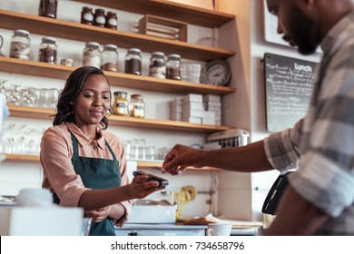 Customer using a bank card and nfs technology to pay a barista for a purchase at a cafe