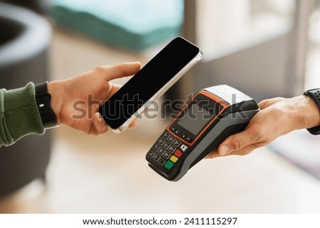 Customer using banking mobile app for payment at cafe restaurant, cashless technology and credit card payment concept. Cropped black man hand hold smartphome next to terminal, contactless payment