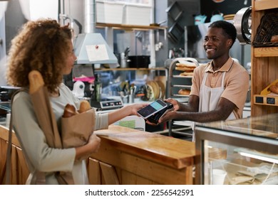 Customer using mobile payment service when buying bread in local bakery - Powered by Shutterstock