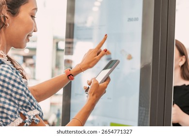 Customer using smartphone and interactive self ordering kiosk at fast food restaurant to choose meal and make contactless payment