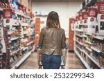 Customer, woman and shopping at grocery store in aisle with wheel cart, food and product. Female person, back and supermarket or convenience shop for retail cost, prices and discounts or promotion