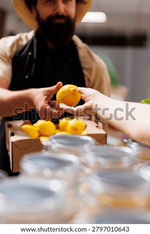 Customer in zero waste shop talking with shopkeeper, inquiring about freshly received batch of handpicked organic fruits. Environmentally friendly client in eco store asking for natural products