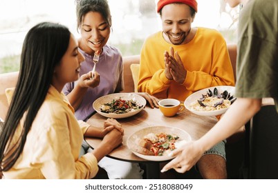 Customers enjoying a meal in a modern cafe, chatting happily. A diverse group of friends sharing salads and pasta, with natural light streaming in - Powered by Shutterstock