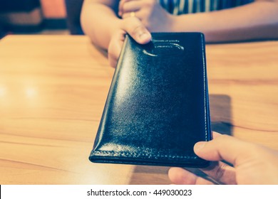 The Customer's Hand Receives A Bill And Receipt From The Waitress For Dinner To Check The Costs That Must Be Paid In The Restaurant. Black Leather Tray With Preparing The Pay To Be Taken To The Table.