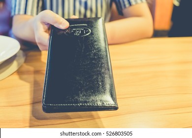 The Customer's Hand Receives A Bill And Receipt From The Waitress For Dinner To Check The Costs That Must Be Paid In The Restaurant. Black Leather Tray With Preparing The Pay To Be Taken To The Table.