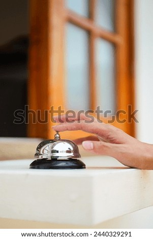 A customer's hand is ringing bell which is placed on the counter at the coffee or restaurant cafe. Action for business concept scene. Close-up and selective focus.