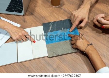 Customers reviewing and comparing tile samples on a wooden table, pointing and discussing colors, textures and patterns while planning flooring and wall choices for a home remodel
