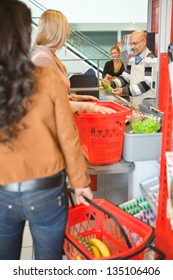 Customers With Shopping Baskets Standing In Line At Checkout Counter In Supermarket