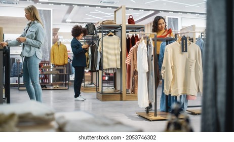 Customers Shopping In Modern Clothing Store, Retail Sales Associate Assists Client. Diverse People In Fashionable Shop, Choosing And Buying Stylish Clothes, Colorful Brand Designs, Quality Materials.