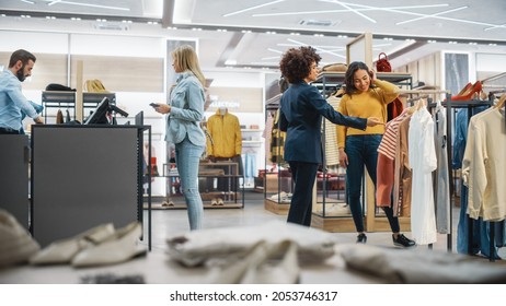 Customers Shopping In Modern Clothing Store, Retail Sales Associate Assists Client. Diverse People In Fashionable Shop, Choosing And Buying Stylish Clothes, Colorful Brand Designs, Quality Materials.