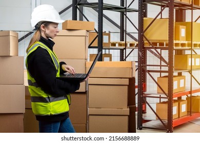 Customs clearance. Girl with laptop in warehouse. Woman works at customs. Woman is using portable computer. Passage of goods across border. Customs officer in reflective vest. Female warehouse rack