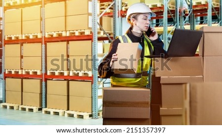 Customs warehouse. Warehouse worker talking on phone. Girl in yellow vest looks at laptop. Woman works in customs warehouse. Customs officer next to boxes. Shelving with parcels in background