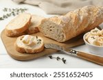 Cut baguette with butter and herbs on white wooden table, closeup