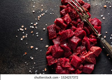 Cut beef into small pieces with sea salt, dried herbs and chili peppers on dark slate or concrete   background. Top view. - Shutterstock ID 1524257372