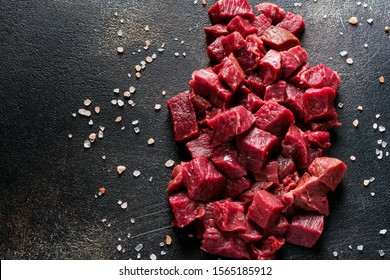 Cut beef into small pieces with sea salt, dried herbs and chili peppers on dark slate or concrete   background. Top view. - Shutterstock ID 1565185912