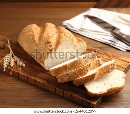 Cut bread loaf, spikelets and knife on wooden table, closeup