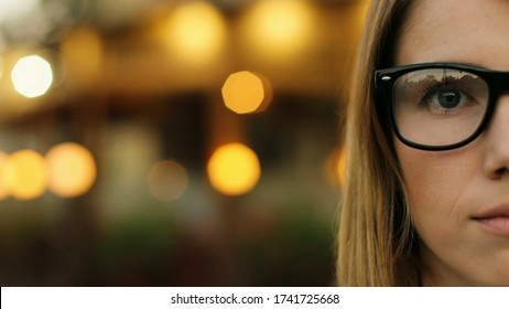 Cut face portrait of happy attractive young woman stylish glasses looking at the camera and smiling in the city street. Close up. Half face portrait.