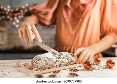 cut festive traditional German Stollen pie into pieces. girl in festive dress cuts stollen with knife in kitchen on christmas eve