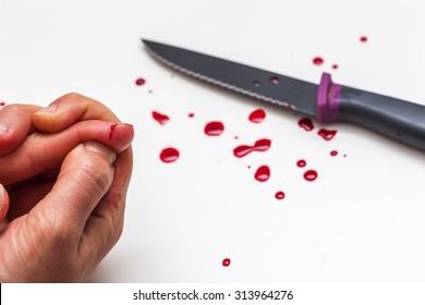 A Cut Of Finger While Cooking. Hand, Knife And Drops Of Blood On A White Surface