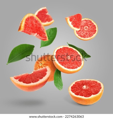 Cut fresh grapefruits and green leaves flying on grey background