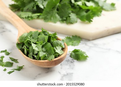 Cut fresh green cilantro and wooden spoon on white marble table, closeup. Space for text