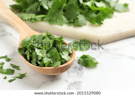 Cut fresh green cilantro and wooden spoon on white marble table, closeup. Space for text