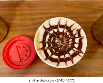 Cut Of To Go Coffee On A Wooden Table With A Beautiful Design Made Of Chocolate. Red Top Upside Down On The Table. 