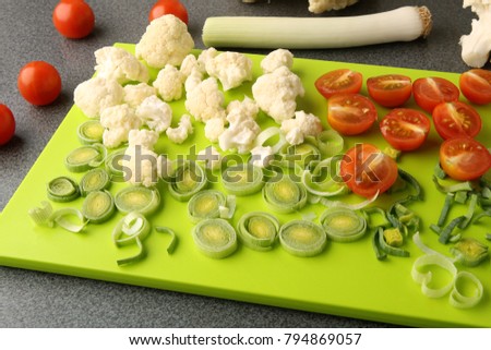 Cut leeks, cherry tomatoes and cauliflower on cutting board. Fresh vegetables sliced on bright green board.