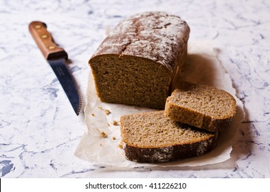 Cut loaf of rye bread on paper. Concrete background. Selective focus.