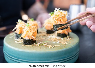 Cut Maki Salmon Sushi Rolls And Spicy Mayo On Turquoise Plate And Hand Of Man With Chopsticks Holding One Piece. Japanese Fancy Restaurant, Gourmet Food Concepts