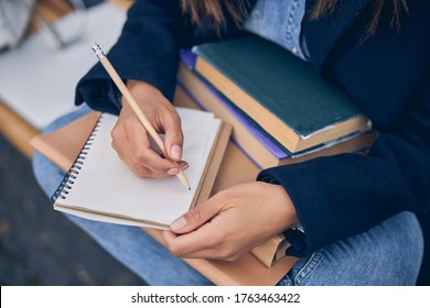 Cut Off Photo Of Female In Jeans Sitting And Writing With Pencil In Notebook