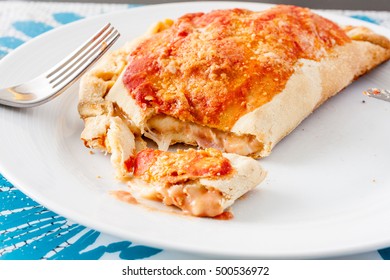 A Cut Open Calzone, A Type Of Folded Pizza, Showing The Melted Oozing Cheese On A White Plate