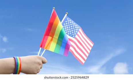 Cut out of hand holding both the LGBT flag and the American flag, set against blue sky background with clipping paths. The symbolizing unity, diversity, and inclusion. - Powered by Shutterstock