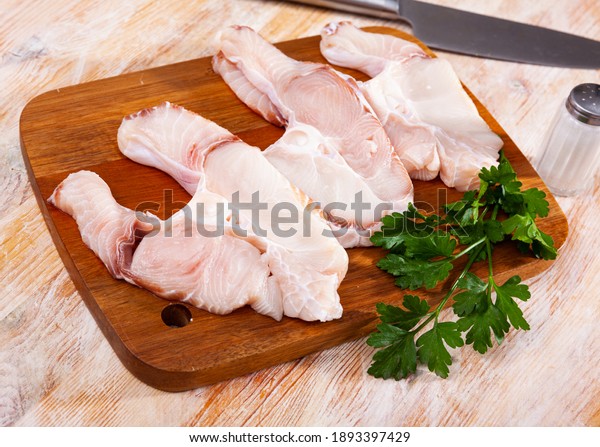 Cut pieces of fresh blue shark on wooden\
surface with greens prepared for\
cooking