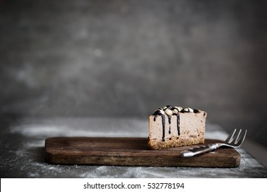 Cut of raw chocolate mousse cake with cashew, hazelnuts and dark chocolate glaze topping on a wooden and grey background. Vegan sugar gluten free dessert. Dark food photography. Copy space, horizontal