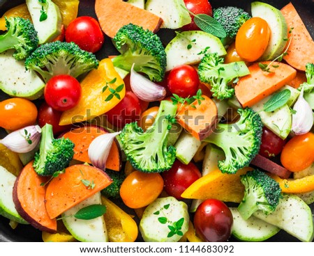 Cut seasonal raw vegetables - sweet potatoes, broccoli, bell peppers, zucchini, tomatoes, onions, garlic with spices and herbs. Ingredients to prepare vegetable side dish. Healthy vegetarian food 
