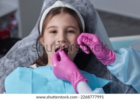 Cut view hands in latex gloves to floss child front teeth. Woman hold dental tools beside
