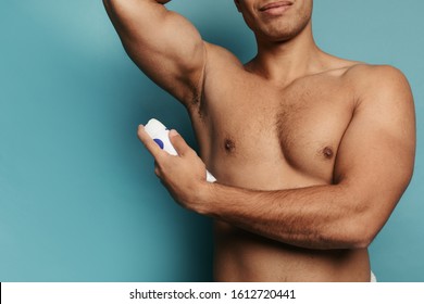 Cut view of muscled strong man's body. Young arabian guy using spray deodorant. Advertisement. After shower hygeine. Isolated over background