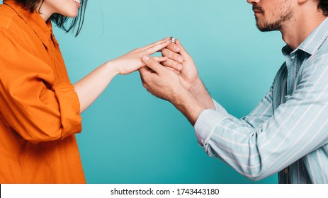 Cut View Of Proposal Moment Where Guy Put On Ring On Girl's Finger. Engagement Time For Young Couple. Love Each Other And Getting Married Soon. Isolated Over Blue Background