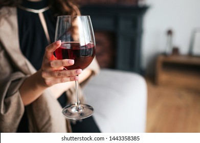 Cut view of woman's hand holding glass of red wine. Model wear black dress and brown shawl. Woman in living room alone.