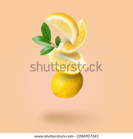 Cut and whole fresh lemons with green leaves falling on pale coral background