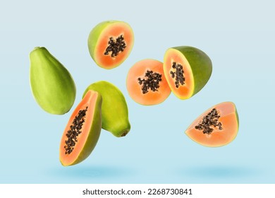 Cut and whole papaya fruits falling on pale light blue background
