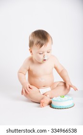 a cute 1 year old sits in a white studio setting. The boy is ready to go in for more cake. He is only dressed in a white diaper