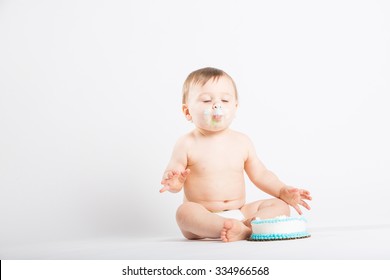 a cute 1 year old sits in a white studio setting. The boy is enjoying his birthday cake with his eyes closed. He is only dressed in a white diaper