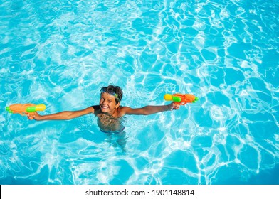 Cute 10 years old boy stand in the water of swimming pool playing with water-pistols