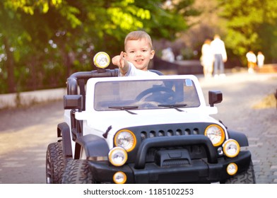 Cute 2 Year Old Boy In A White T Shirt Is Riding A White Electric Car In The Park